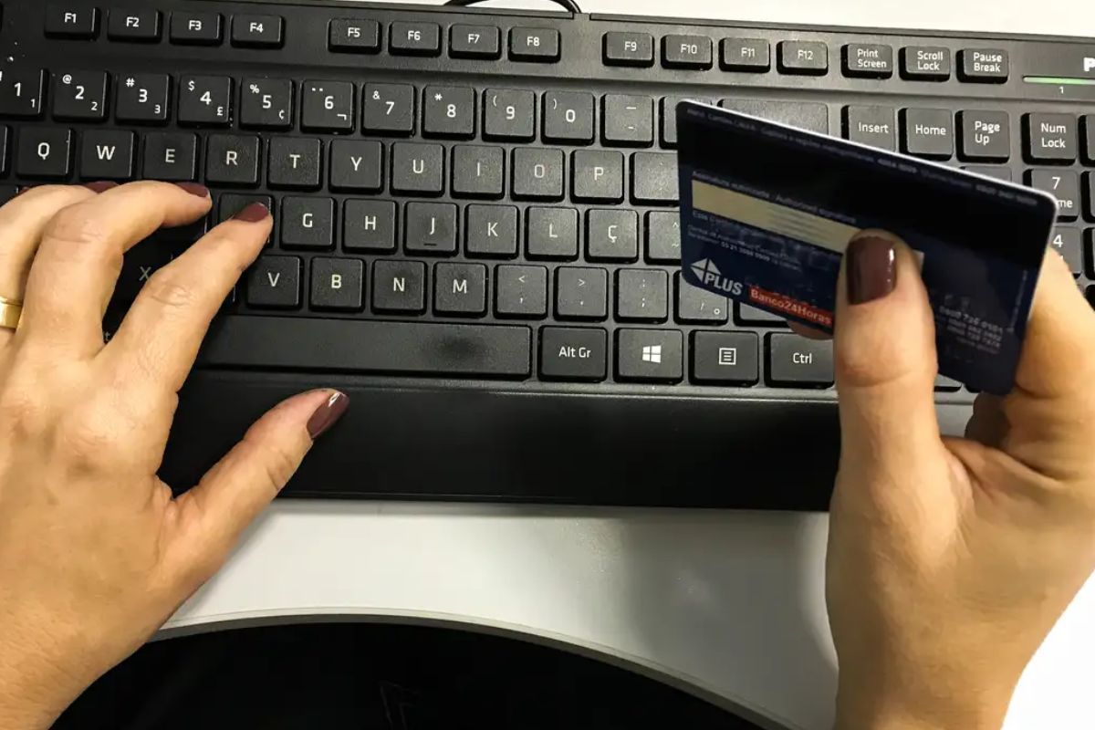 foto de mulher segurando cartão enquanto mexe no computador. imagem ilustra endividamento das mulheres.